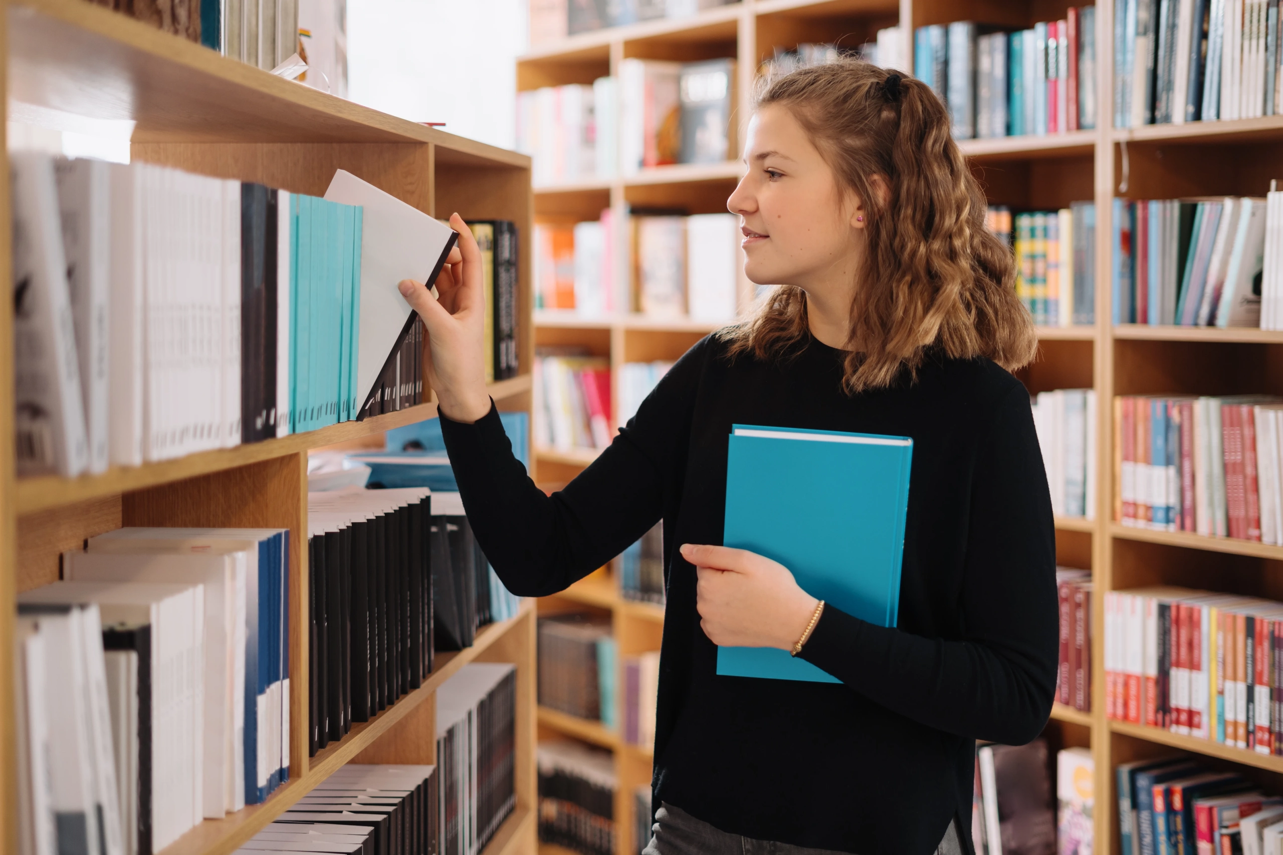 Teenager girl picking book library shelf